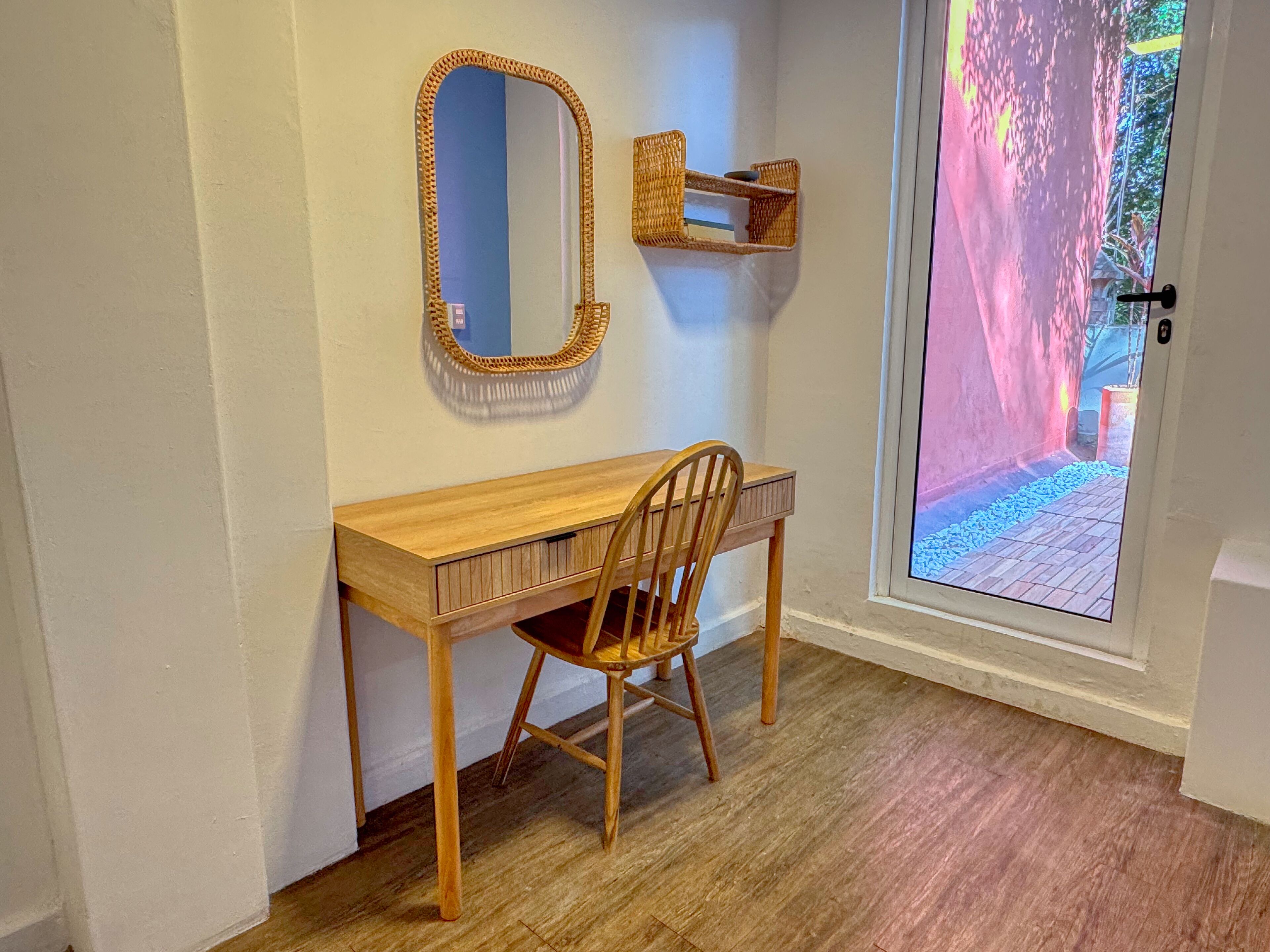 Une pièce avec un bureau en bois, une chaise, un miroir et une fenêtre donnant sur un jardin.
