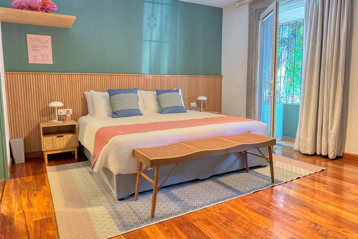 Une chambre à coucher bien rangée, avec un lit, des tables de chevet, une commode, un banc et une fenêtre avec des rideaux.