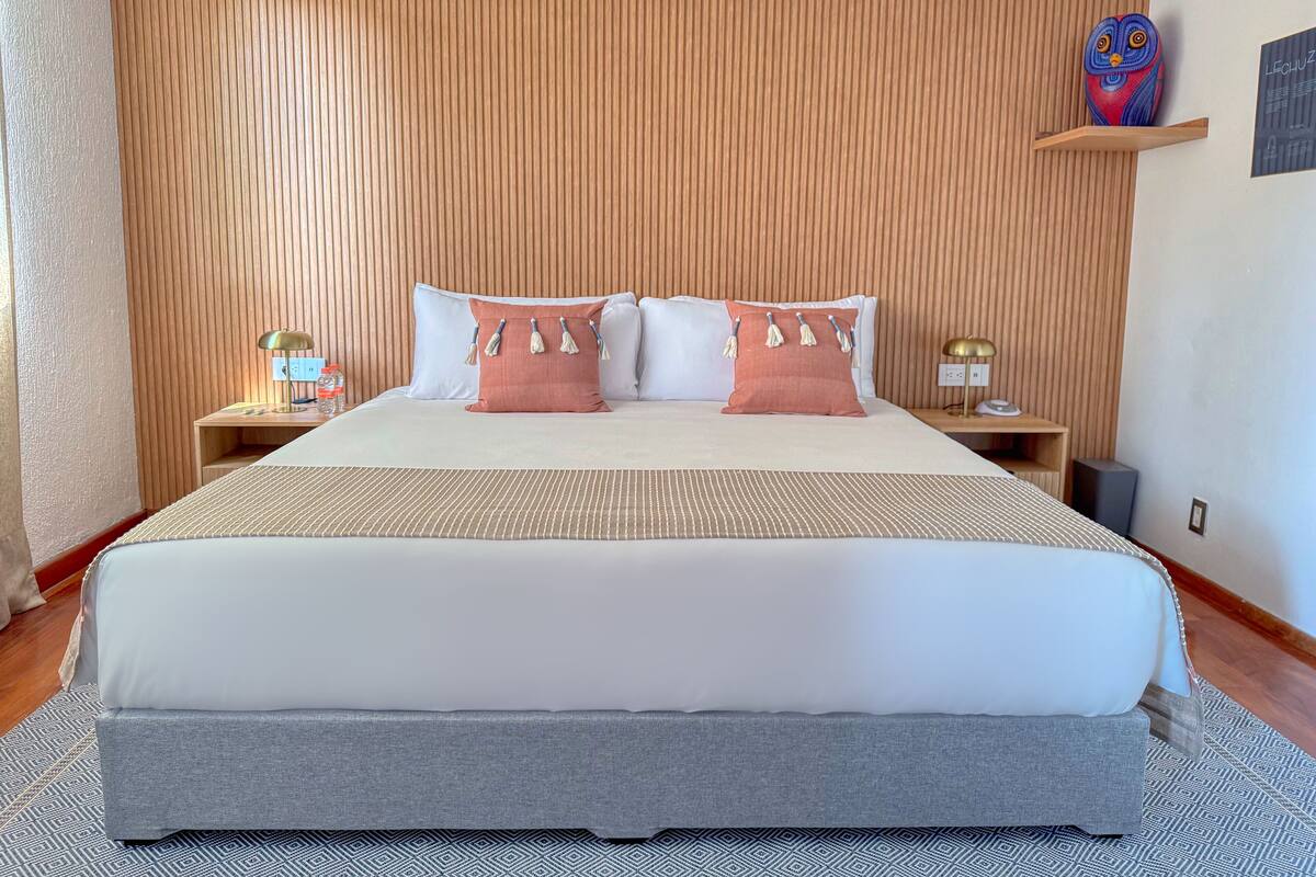 Une chambre d’hôtel bien aménagée, avec un grand lit, deux tables de chevet et un mur recouvert de lambris en bois.
