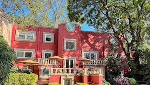 Un edificio rojo con numerosas ventanas, un balcón con barandilla y un pequeño jardín con un sendero que lleva a la entrada.