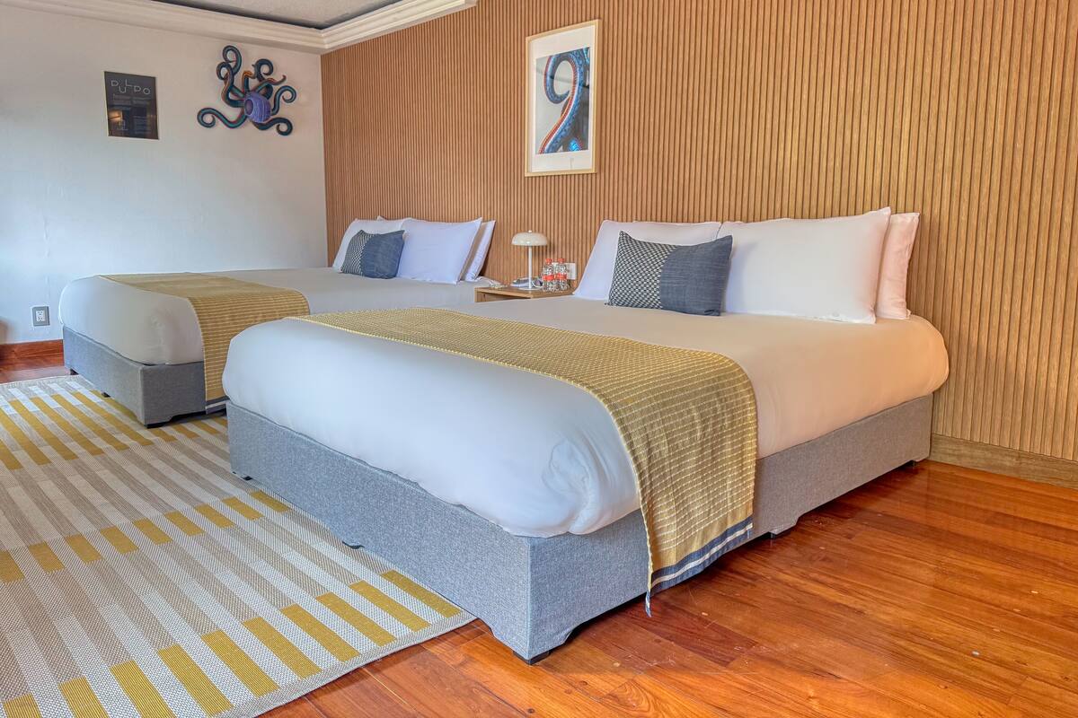 Une chambre d’hôtel avec deux lits, un mur recouvert de panneaux en bois, un tableau encadré et un tapis à rayures.