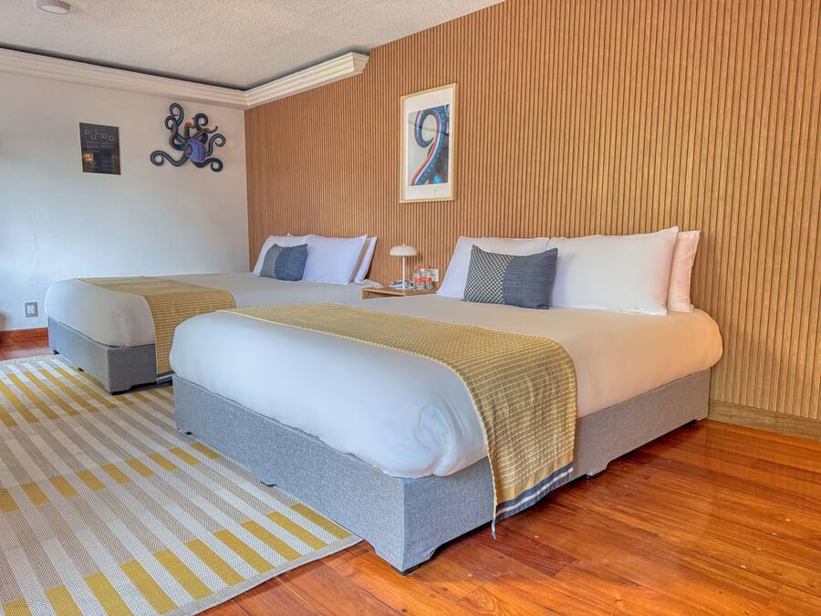 A hotel room with two beds, a wooden panel wall, a framed artwork, and a striped rug.