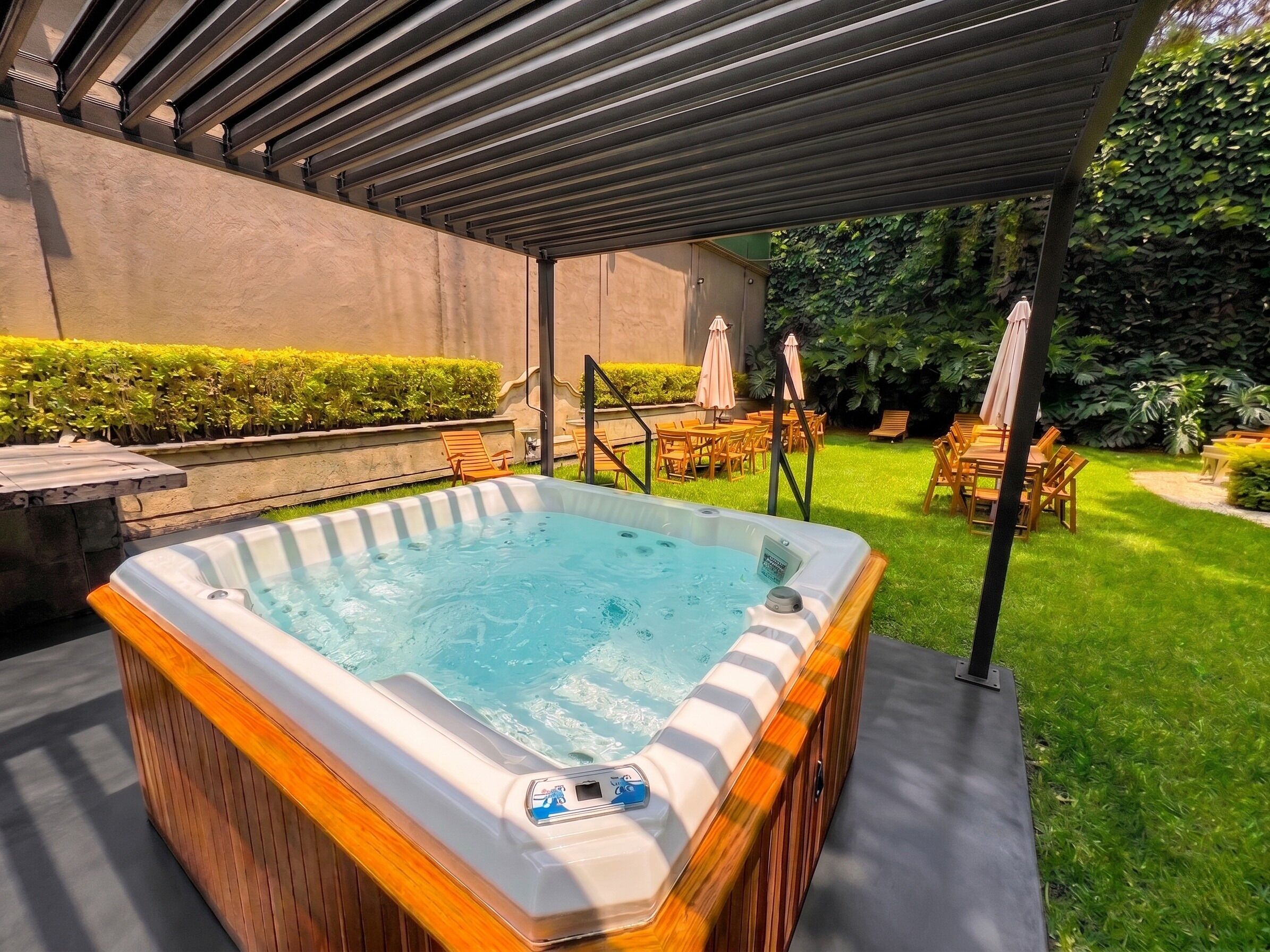 Een bubbelbad in een open omgeving met een overdekt terras, omringd door stoelen en parasols.
