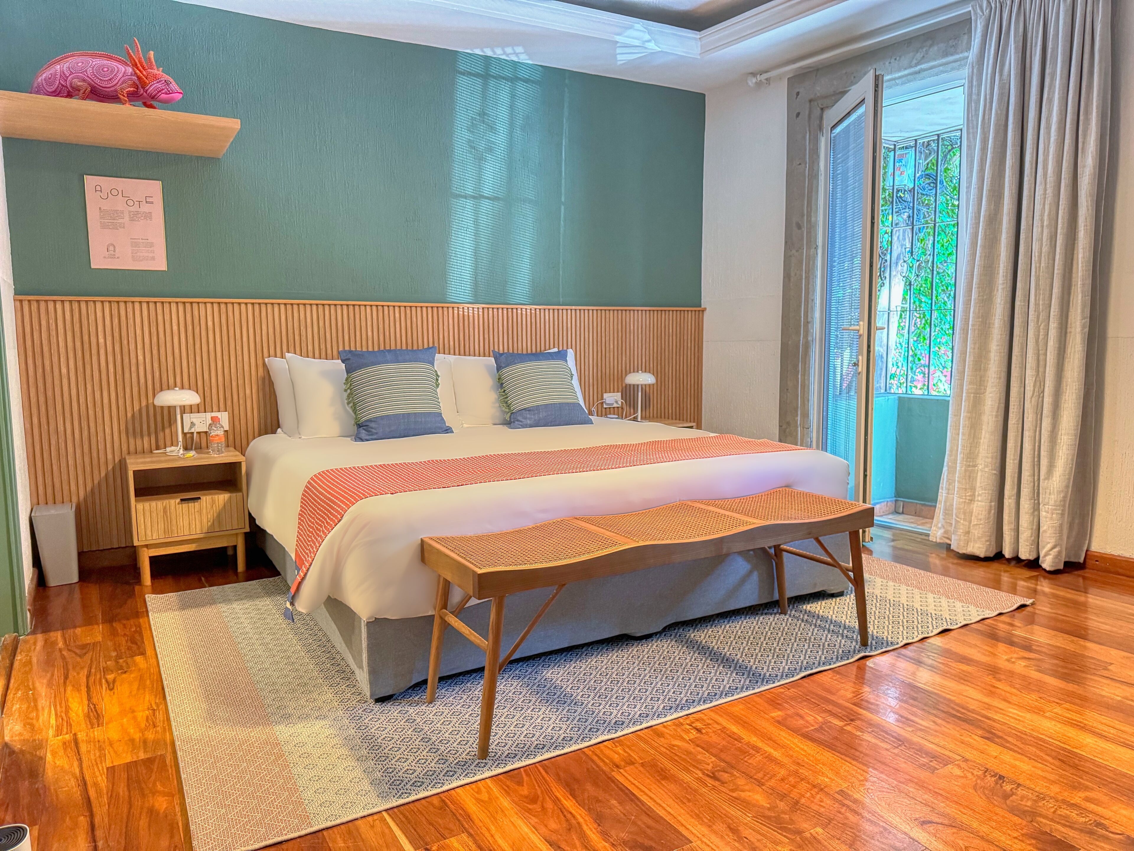 Een netjes opgemaakt slaapkamer met een bed, nachtkastjes, een bankje en een raam met gordijnen.