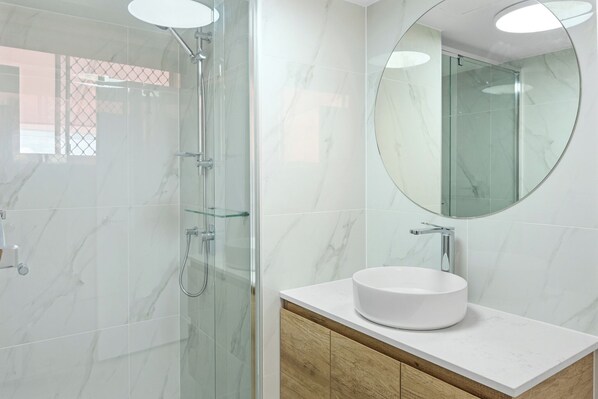 A modern bathroom with a glass-enclosed shower, a round white sink, and a large mirror. - Coastal Delight at Kupari (Surfers Paradise)