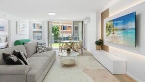 Een moderne woonkamer met een bank, salontafel en een aan de muur bevestigde televisie.