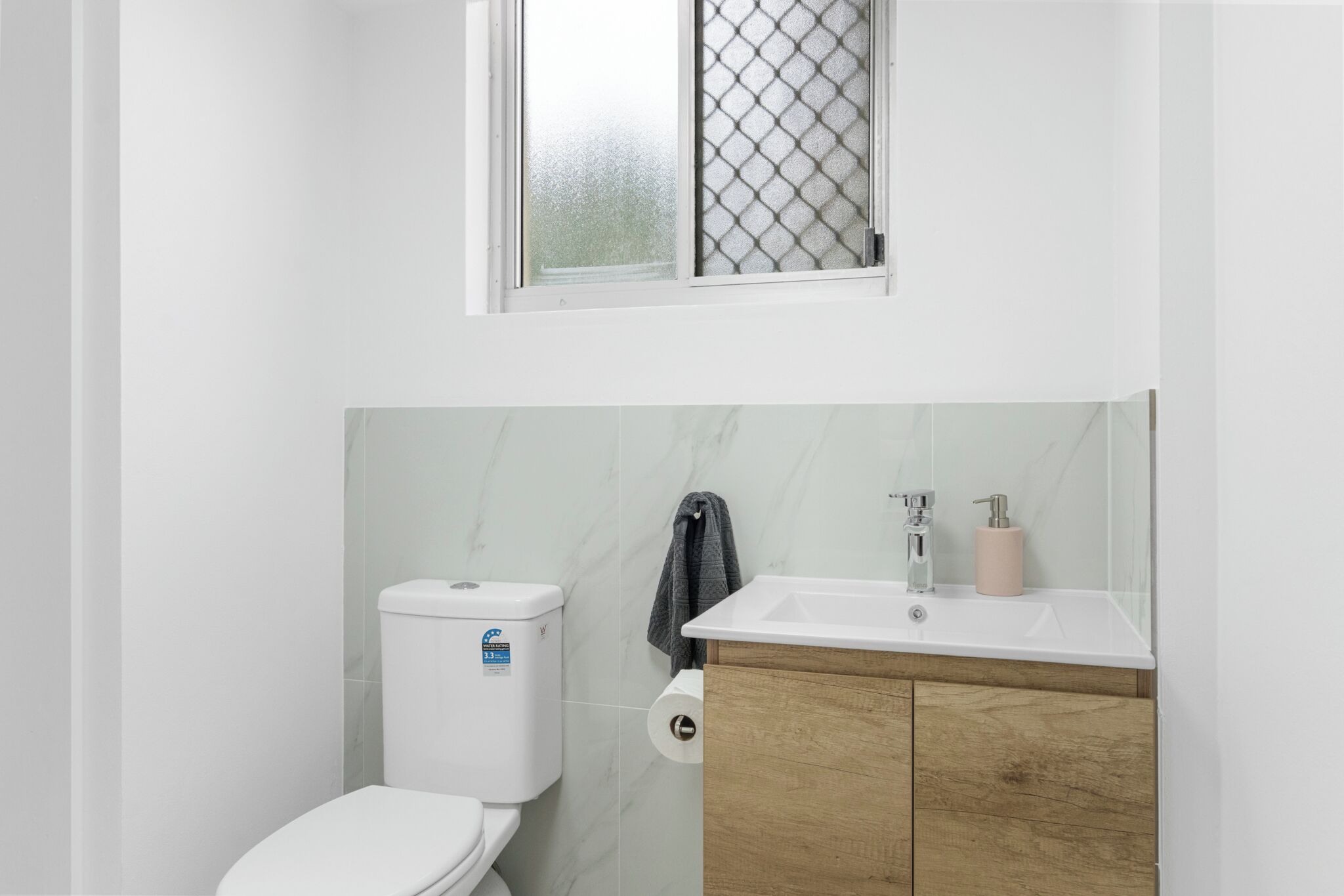 Un baño con inodoro, lavabo y ventana con diseño de vidrio esmerilado.