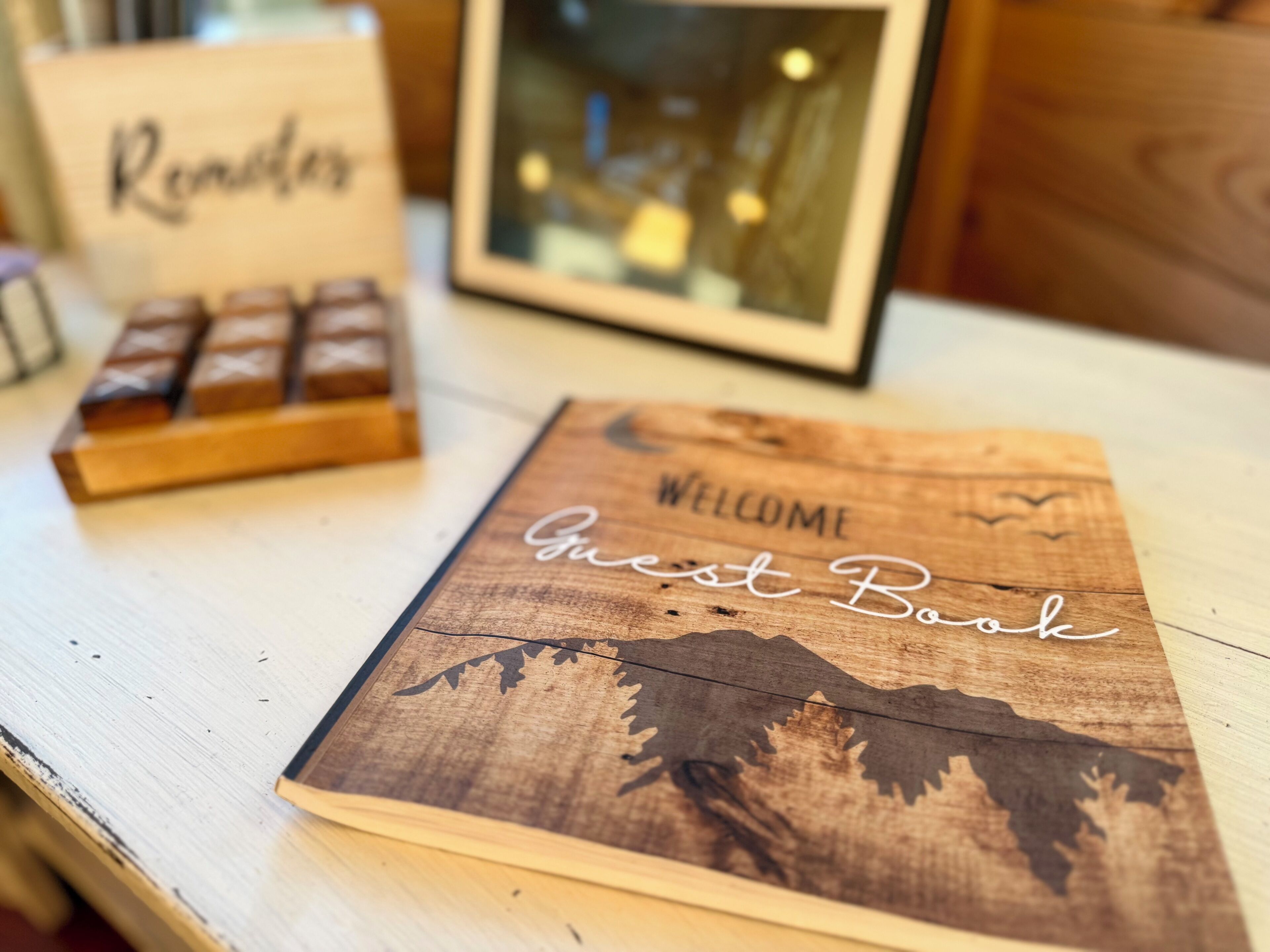 A wooden welcome book with a forest silhouette, a framed picture, and a sign with the word 'Rendezvous'.