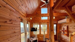 A cabin with wooden walls, a ceiling fan, a TV, a sofa, and a window with curtains.