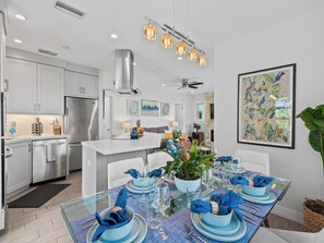 Eine moderne Küche mit Edelstahlgeräten, ein Essbereich mit blau gedecktem Tisch und ein großes Vogelgemälde an der Wand.