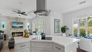 A modern kitchen with a large island, a fireplace, and a dining area with a view of greenery. - New Heated Pool Home in Fort Lauderdale,Charming Tropical Retreat Near Beaches, Shopping & Dining! (Fort Lauderdale)