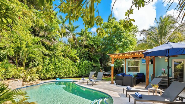 A swimming pool with lounge chairs and a covered seating area surrounded by lush greenery. - New Heated Pool Home in Fort Lauderdale,Charming Tropical Retreat Near Beaches, Shopping & Dining! (Fort Lauderdale)