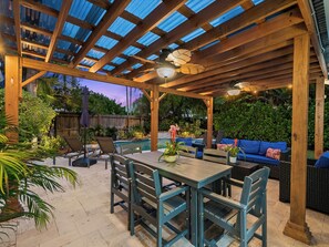Ein überdachter Patio-Bereich mit Pool, Holzmöbeln und Topfpflanzen.