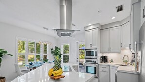 A modern kitchen with white cabinetry, stainless steel appliances, and a central island with a fruit bowl. - New Heated Pool Home in Fort Lauderdale,Charming Tropical Retreat Near Beaches, Shopping & Dining! (Fort Lauderdale)