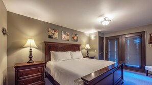 Une chambre à coucher avec un grand lit, deux tables de chevet avec des lampes, une tête de lit en bois et une porte avec des stores.