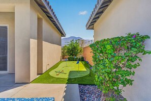 Una propiedad residencial con entrada pavimentada, un pequeño césped con putting green y un muro de ladrillo.