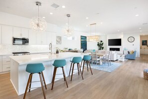 A modern kitchen with a central island, bar stools, and a dining area with a TV and seating.