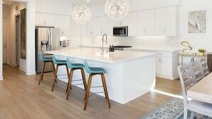 A modern kitchen with white cabinetry, a central island with bar stools, stainless steel appliances, and pendant lighting. - Exclusive Oasis: Pool, Spa & Golf Access (La Quinta)