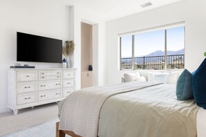 A bedroom with a large bed, a television on a dresser, and a window with a mountain view.
