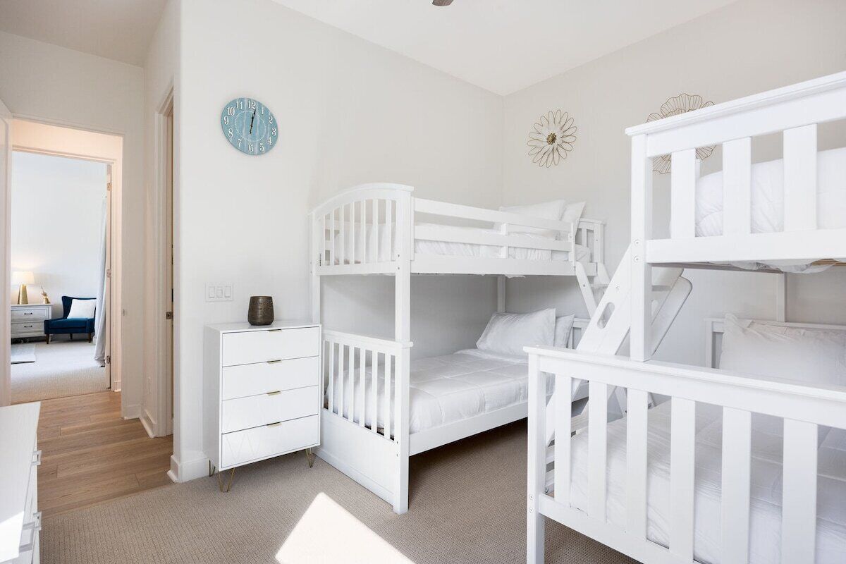 A child's room with bunk beds, a white dresser, a clock, and a wall decoration.