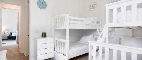 Ein Kinderzimmer mit Etagenbetten, einer weißen Kommode, einer Uhr und einer Wanddekoration.