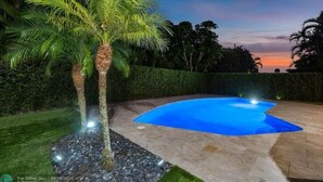 A swimming pool with a curved edge, surrounded by a stone patio and a well-maintained lawn.