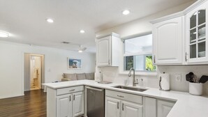 A modern kitchen with white cabinetry, a built-in dishwasher, and a large window providing natural light.