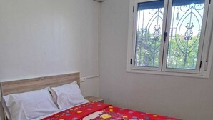 A bedroom with a bed, white walls, an air conditioning unit, a window with decorative iron bars, and a patterned rug. - Dar Latifa (Tinghir)