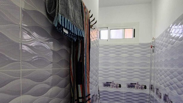 A bathroom with a textured wall design, a towel rack, and a small shelf with toiletries. - Dar Latifa (Tinghir)