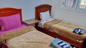 A room with two wooden beds, each with a headboard, a small table, and a window with metal bars. - Dar Latifa (Tinghir)