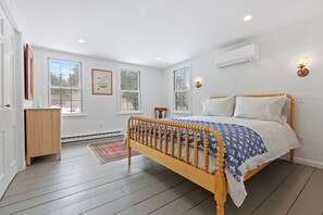 Ein Schlafzimmer mit einem hölzernen Bett, weißen Wänden und großen Fenstern.