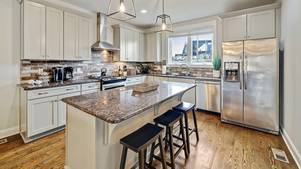Una cocina moderna con armarios blancos, encimeras de granito, electrodomésticos de acero inoxidable y una isla grande con taburetes de bar.