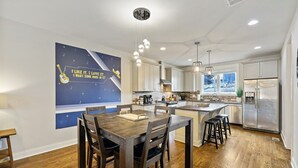 Una cocina moderna con armarios blancos, un refrigerador de acero inoxidable y un comedor con mesa y sillas de madera.