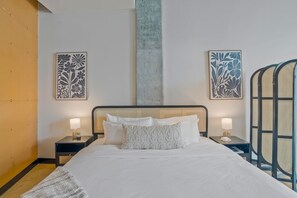 Ein ordentlich bezogenes Bett mit weißen Leinen, zwei Nachttische mit Lampen sowie zwei an der Wand befestigte Kunstwerke.