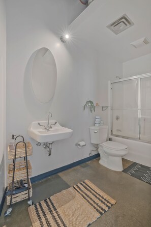 Ein modernes Badezimmer mit Waschbecken, Toilette und Dusche. Über dem Waschbecken hängt ein Spiegel und an der Wand steht eine kleine Pflanze.