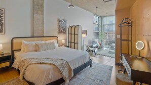 Ein modernes Schlafzimmer mit einem großen Bett, Nachttischen, einem Schreibtisch mit Spiegel und Blick auf die Stadt durch große Fenster.