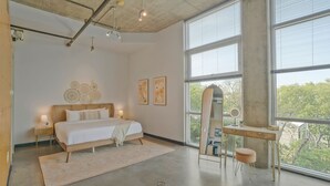 Camera da letto moderna con un letto grande, comodini, una toeletta con specchio e un'ampia finestra che si affaccia su alberi.