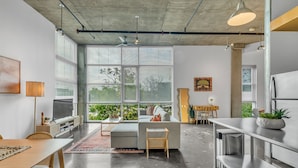 Ein moderner Wohnraum mit großem Fenster, einer Couch, einem Esstisch und einer Küchenzeile.