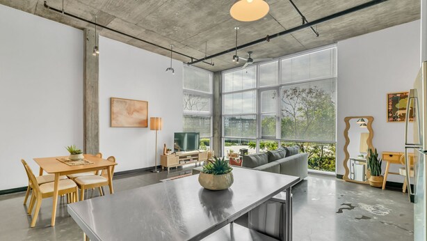 Ein modernes Wohnzimmer mit Essbereich, großen Fenstern und einer Beton Decke.