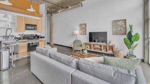 A modern living space with a kitchen, sofa, TV, and decorative plants. - Downtown 1 Bedroom Loft in the Gulch (Nashville)