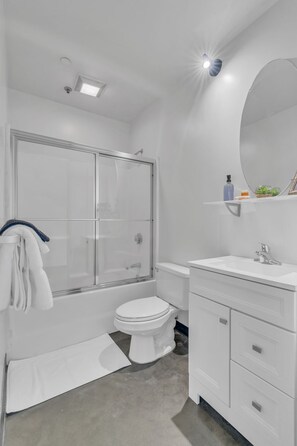 A modern bathroom with a glass-enclosed shower, a white toilet, and a vanity with a mirror. - Downtown 1 Bedroom Loft in the Gulch (Nashville)