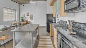 A modern kitchen with stainless steel appliances, wooden cabinets, and a large window. - Downtown 1 Bedroom Loft in the Gulch (Nashville)