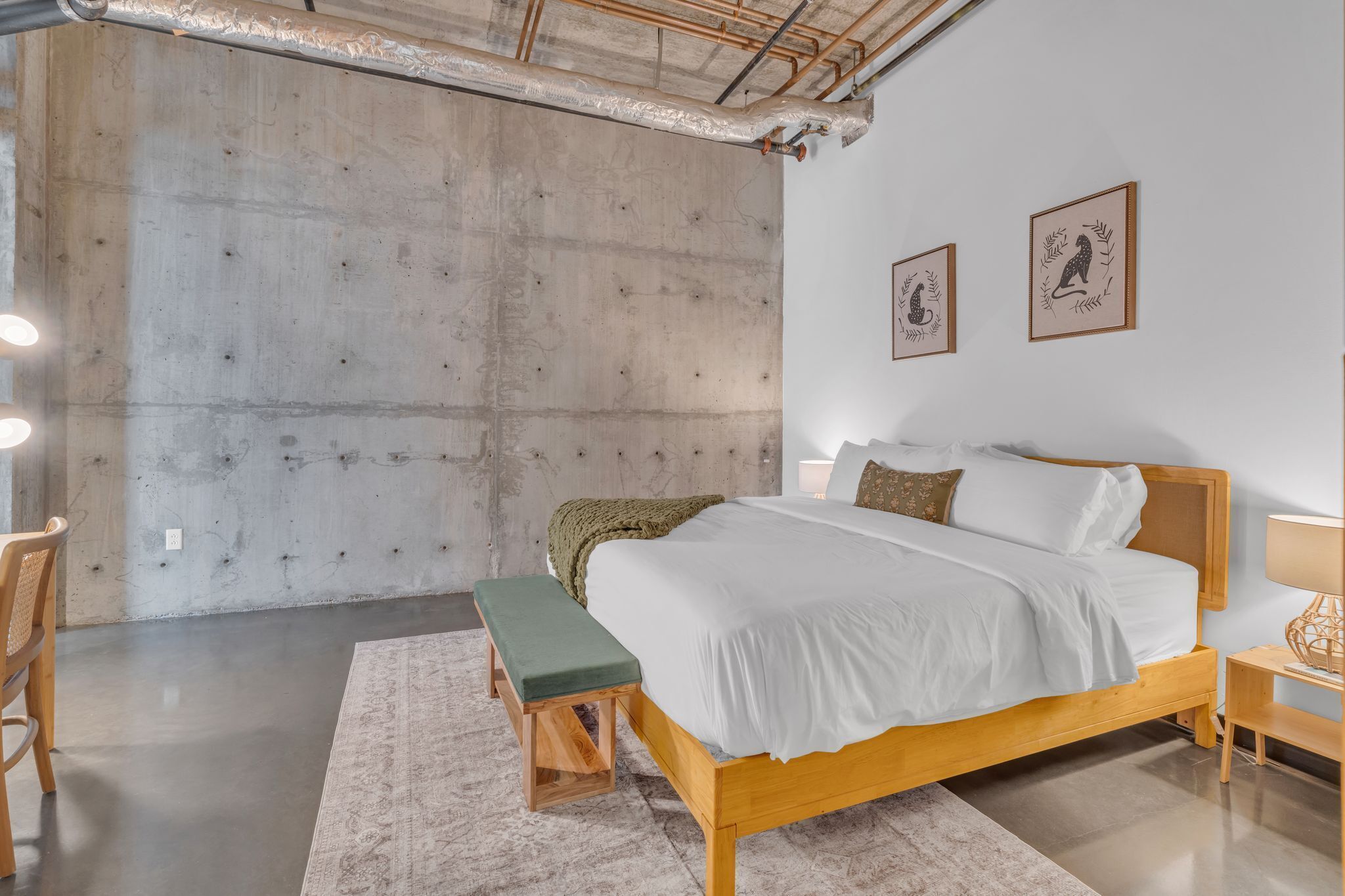Une chambre moderne avec un grand lit, un banc et un mur en béton.