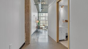 A hallway leading to a bathroom with a white sink and a mirror. - Downtown 1 Bedroom Loft in the Gulch (Nashville)