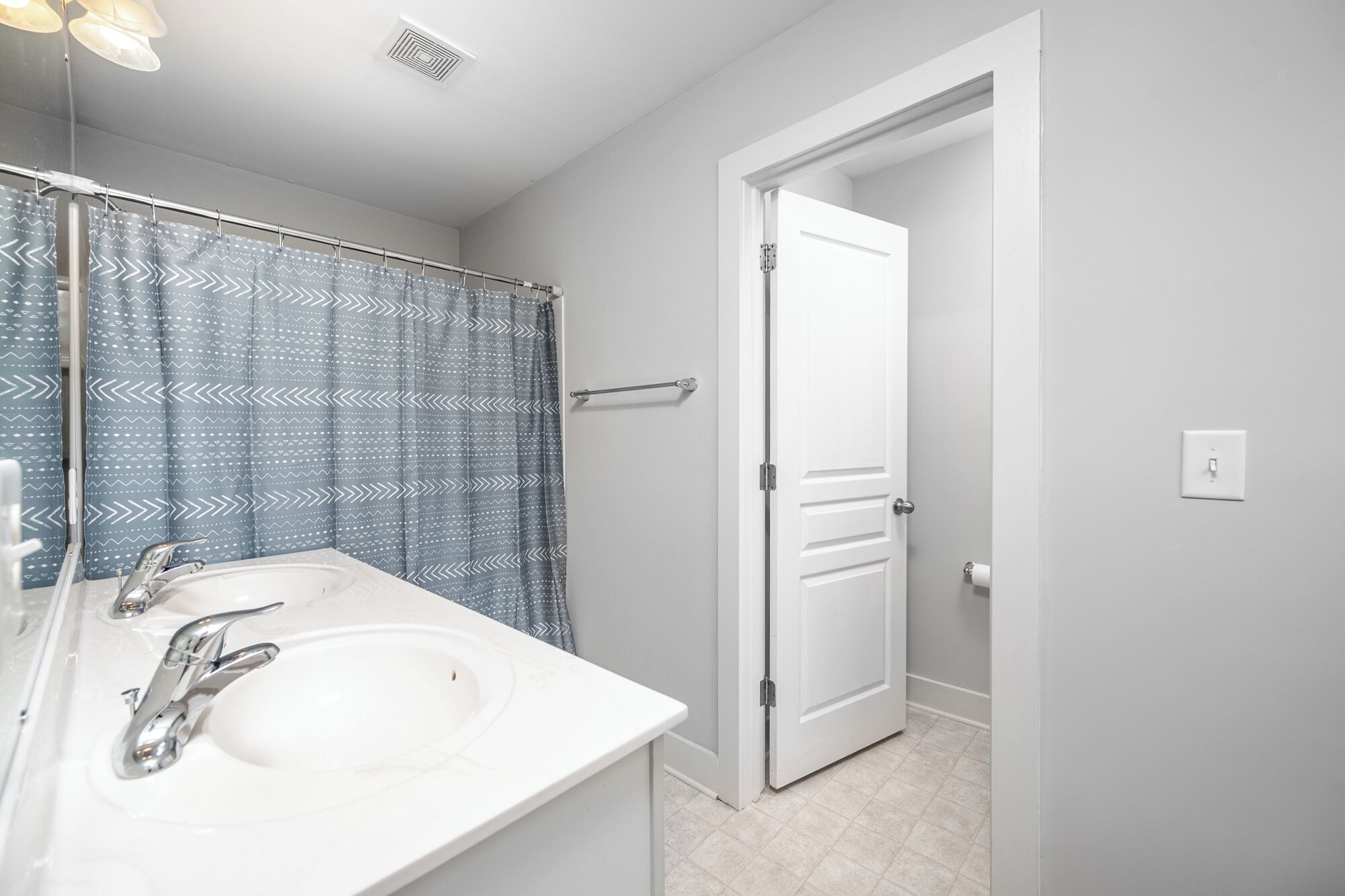A bathroom with a white sink, two faucets, a shower curtain with a zigzag pattern, and a white door.