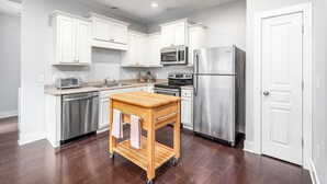 A modern kitchen with white cabinets, stainless steel appliances, and a wooden cart. - Adorable home in fantastic location near restaurants and Duke! (Durham)