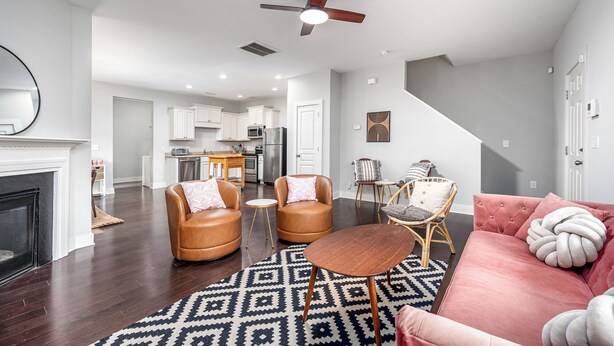 A modern living room with a fireplace, leather armchairs, a pink sofa, and a dining area with a kitchen in the background. - Adorable home in fantastic location near restaurants and Duke! (Durham)