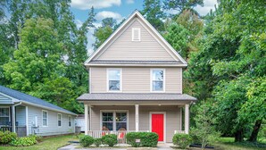 A two-story house with a red door, a front porch, and a small garden area. - Adorable home in fantastic location near restaurants and Duke! (Durham)