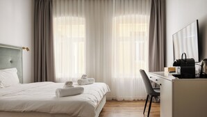 A hotel room with a bed, a desk, a chair, and a large window with curtains. - Richter Residence 3 (Brașov)