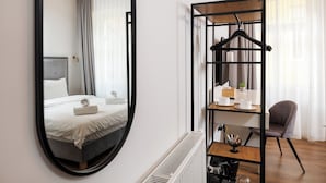 A modern hotel room with a large mirror, a bed with white linens, a wooden headboard, a small table with a plant, and a chair. - Richter Residence 6 (Brașov)